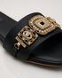 Close up of Aurista black flat sandals highlighting intricate antique gold embellishments and premium craftsmanship.