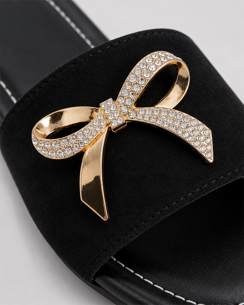Close up of Aveen black flat sandals featuring embellished bow detail