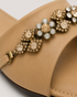 Close up of beige flat sandals highlighting the crystal embellished floral strap and premium craftsmanship.