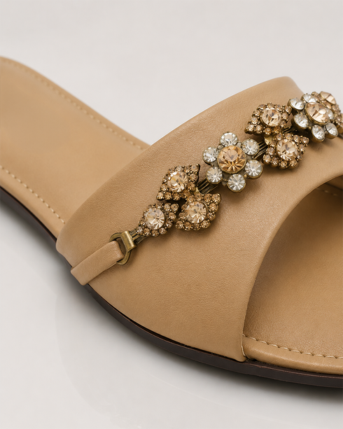 Close up of beige flat sandals highlighting the crystal embellished floral strap and premium craftsmanship.