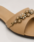 Close up of beige flat sandals highlighting the crystal embellished floral strap and premium craftsmanship.