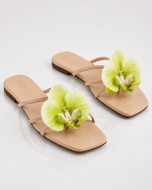Pair of beige floral flat sandals with oversized orchid flower embellishment and padded comfort sole.