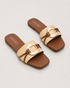 Pair of beige buckle flat sandals with oversized metallic buckle and padded comfort sole.