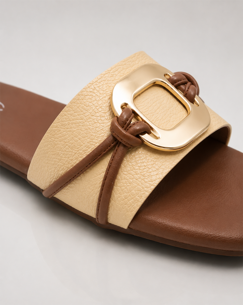 Close up of beige buckle flat sandals highlighting the oversized metallic buckle and textured upper.