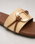 Close up of beige buckle flat sandals highlighting the oversized metallic buckle and textured upper.