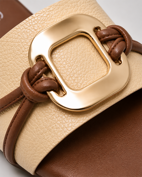 Close up of beige buckle flat sandals highlighting the oversized metallic buckle and textured upper.