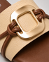Close up of beige buckle flat sandals highlighting the oversized metallic buckle and textured upper.