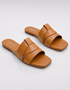 Pair of tan flat sandals with minimalist overlapping straps and cushioned footbed.