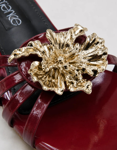 Close up of metallic flower embellishment on Imperial maroon patent flat sandals