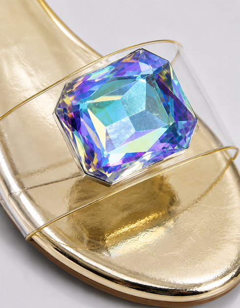 Close-up of oversized iridescent crystal rhinestone on gold flat party sandal