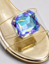 Close-up of oversized iridescent crystal rhinestone on gold flat party sandal
