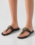 Black sandals with decorative straps worn by a person on a light gray background